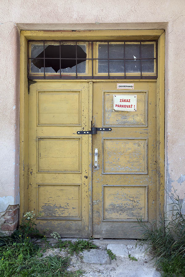 Photo 25435: Worn, panelled, yellow double door with broken, barred top window
