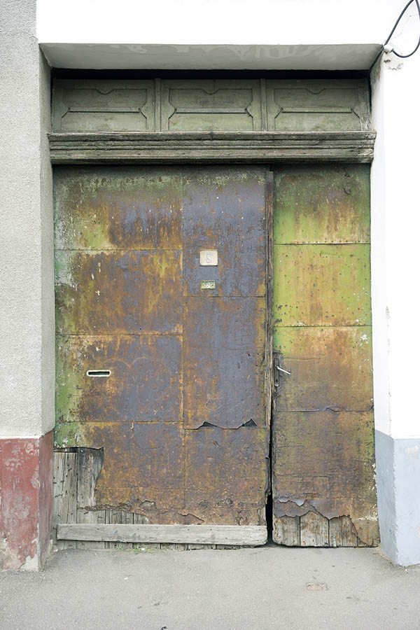 Photo 25763: Decayed gate of unpainted boards covered by yellow, light green, orange, brown and black metal plate