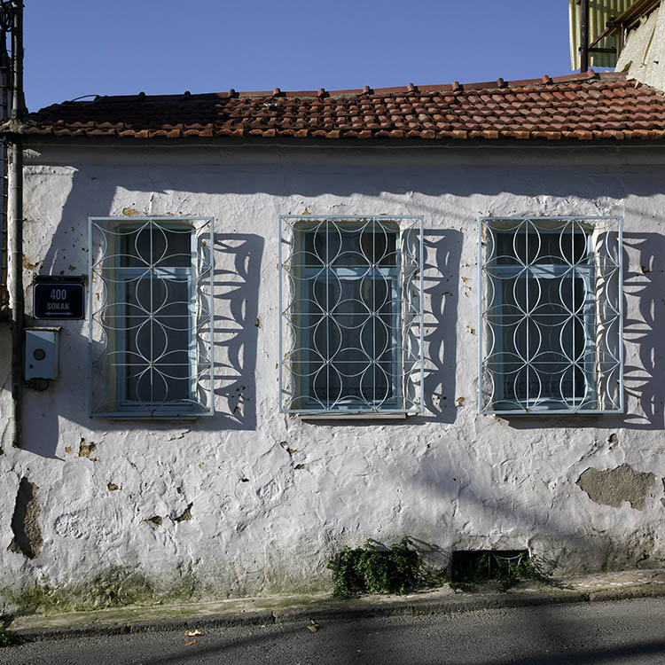 Photo 26521: Worn, white, plastered facade with three light blue, latticed windows