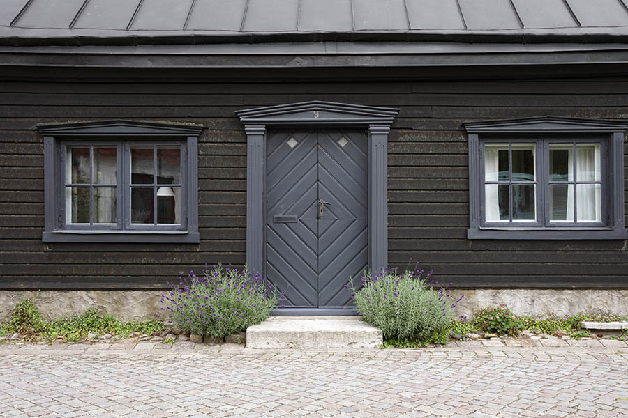 Photo 27090: Facade with grey double door of boards in diamond pattern and carved pilastre. Two windows with two frames and eight panes each.