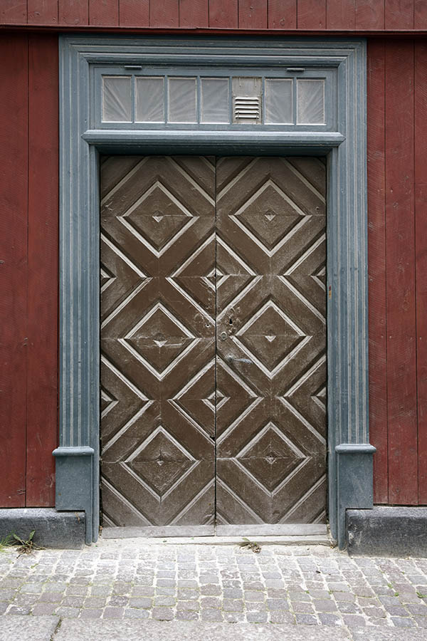 Photo 27284: Worn, brown double door of boards in diamond shape with teal pilastre and top window