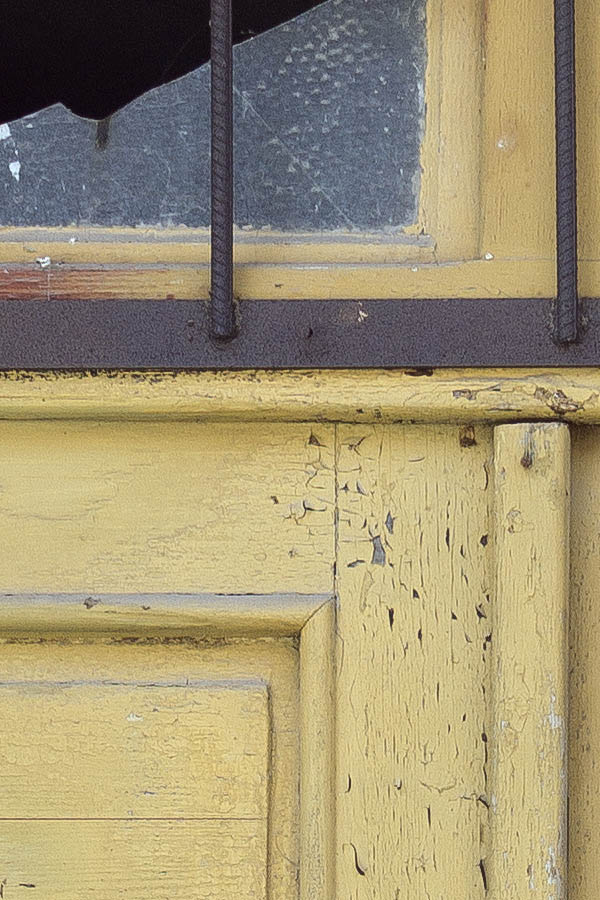 Photo 25435: Worn, panelled, yellow double door with broken, barred top window