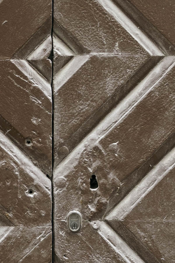 Photo 27284: Worn, brown double door of boards in diamond shape with teal pilastre and top window