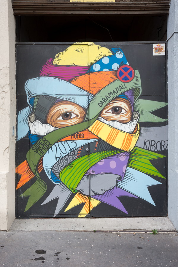 Photo 26160: Metal double door covered with grafitti: A face wrapped in orange, green, blue and yellow strips