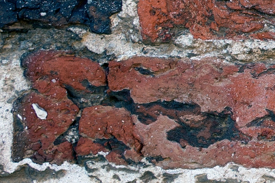 Photo 25293: Worn brick wall with red and black colours.